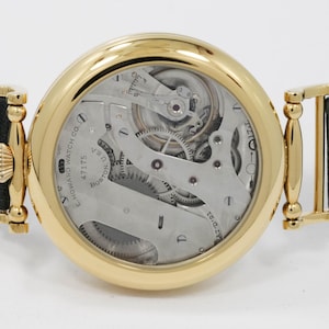 May include: A gold wristwatch with a visible mechanical movement and a teal leather strap. The watch face displays intricate gears and the text "E. HOWARD WATCH CO. BOSTON U.S.A."