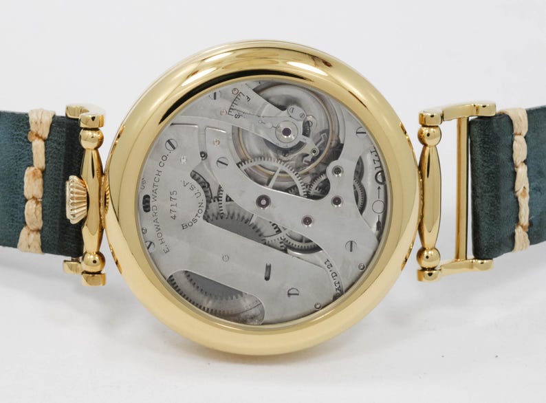 May include: A gold wristwatch with a visible mechanical movement and a teal leather strap. The watch face displays intricate gears and the text "E. HOWARD WATCH CO. BOSTON U.S.A."