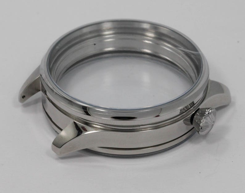 May include: A stainless steel watch case with a clear crystal and a crown. The watch case has a round shape with a polished finish. The case has two lugs for attaching a watch strap.