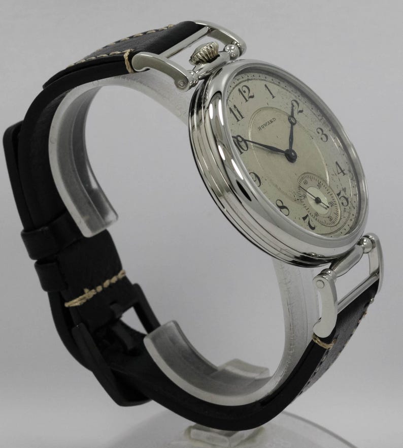 K&ouml;nnte beinhalten: Eine silberfarbene Armbanduhr mit einem runden, cremefarbenen Zifferblatt, schwarzen arabischen Ziffern und dem Schriftzug Howard. Die Uhr hat schwarze Zeiger, ein kleines Hilfszifferblatt auf der Sechs-Uhr-Position und ein schwarzes Lederarmband.