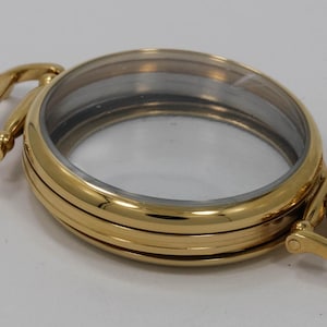 May include: Gold-tone watch case with a clear glass face and a hinged strap.