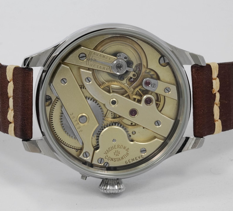 Puede incluir: La parte posterior de un reloj de pulsera plateado con una correa de cuero marr&oacute;n. La esfera del reloj est&aacute; abierta, revelando el intrincado funcionamiento interno del reloj. La esfera del reloj est&aacute; etiquetada como "Vacheron Constantin Geneve".