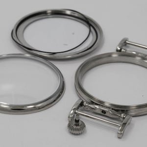 May include: Three silver watch parts, including a round crystal, a bezel, and a case back with a spring bar.