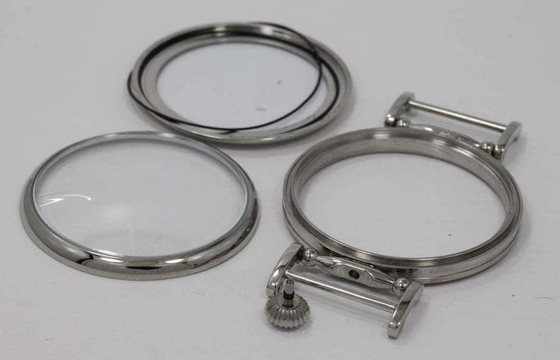 May include: Three silver watch parts, including a round crystal, a bezel, and a case back with a spring bar.