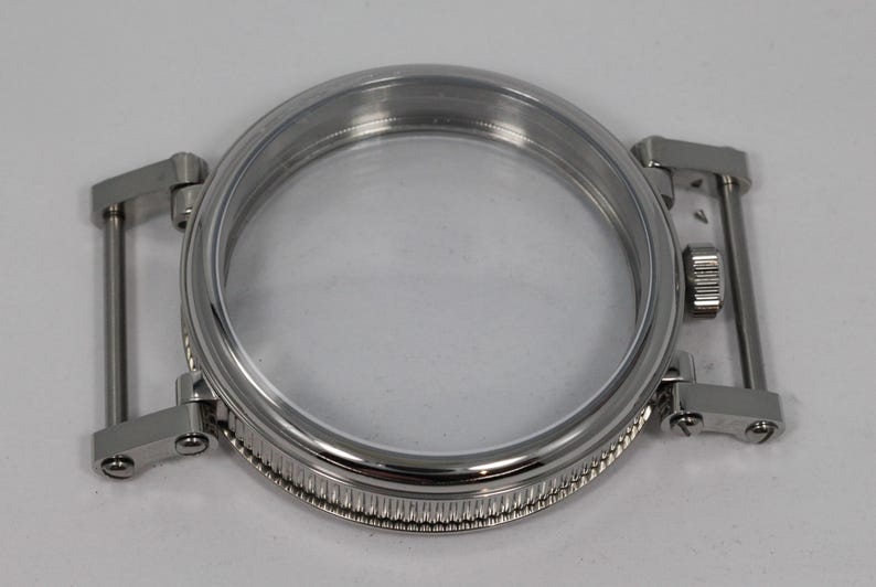 May include: A stainless steel watch case with a clear crystal. The case has a round shape with a ridged bezel and integrated lugs for the watch band. The watch case is designed to hold the watch movement and protect the watch face.