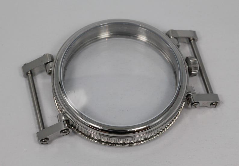 May include: A stainless steel watch case with a clear crystal and integrated lugs. The case has a circular design with a ridged bezel and is ready for a watch movement. The lugs are designed to attach to a watch strap.
