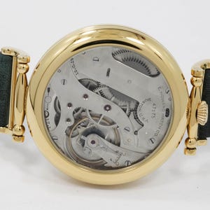 May include: A gold wristwatch showcasing its mechanical workings, with a dark green and blue striped leather strap. The watch face reveals intricate gears and the inscription "E. Howard Watch Co., Boston, U.S."