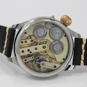 May include: A silver pocket watch with a skeletonized dial, revealing the intricate inner workings of the movement. The watch has a black leather strap with white stitching and a gold-toned crown.