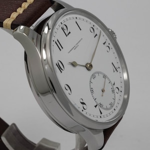 Puede incluir: Un reloj de pulsera plateado con una esfera blanca y marcadores de hora romanos negros. El reloj tiene un peque&ntilde;o subdial en la posici&oacute;n de las 6 en punto y el texto "VACHERON & CONSTANTIN GENEVE" est&aacute; impreso en la esfera.