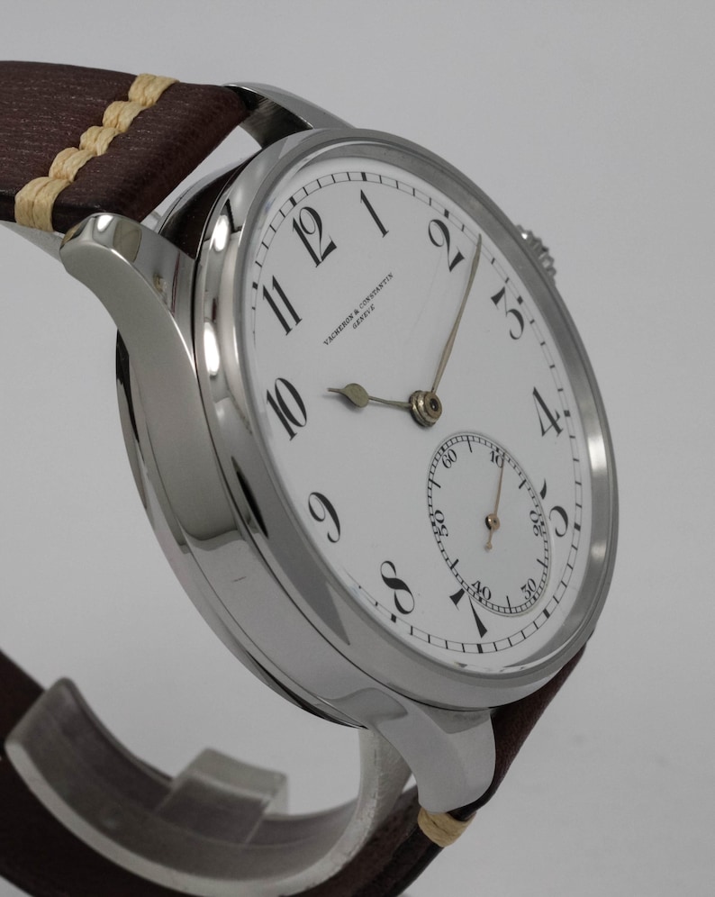 Puede incluir: Un reloj de pulsera plateado con una esfera blanca y marcadores de hora romanos negros. El reloj tiene un peque&ntilde;o subdial en la posici&oacute;n de las 6 en punto y el texto "VACHERON & CONSTANTIN GENEVE" est&aacute; impreso en la esfera.
