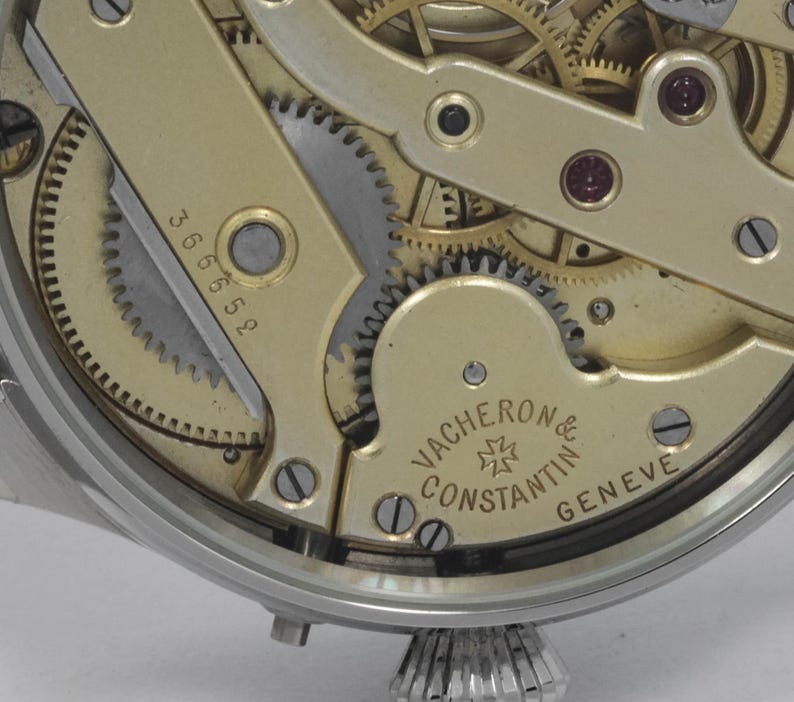 Puede incluir: Primer plano de un movimiento de reloj de tono dorado con engranajes intrincados y la inscripci&oacute;n "VACHERON CONSTANTIN GENEVE" en la parte inferior.