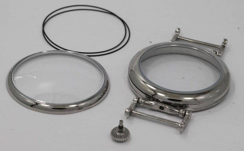 May include: A set of watch parts including a clear glass crystal, a metal case back, a metal strap, and a small metal screw.
