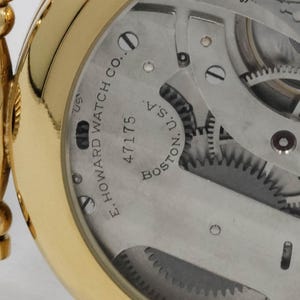 May include: Close-up of a gold pocket watch's inner workings. The watch mechanism is visible, with gears and other components. The text "E. HOWARD WATCH CO. BOSTON. U.S.A." and the number "47175" are printed on the watch face.