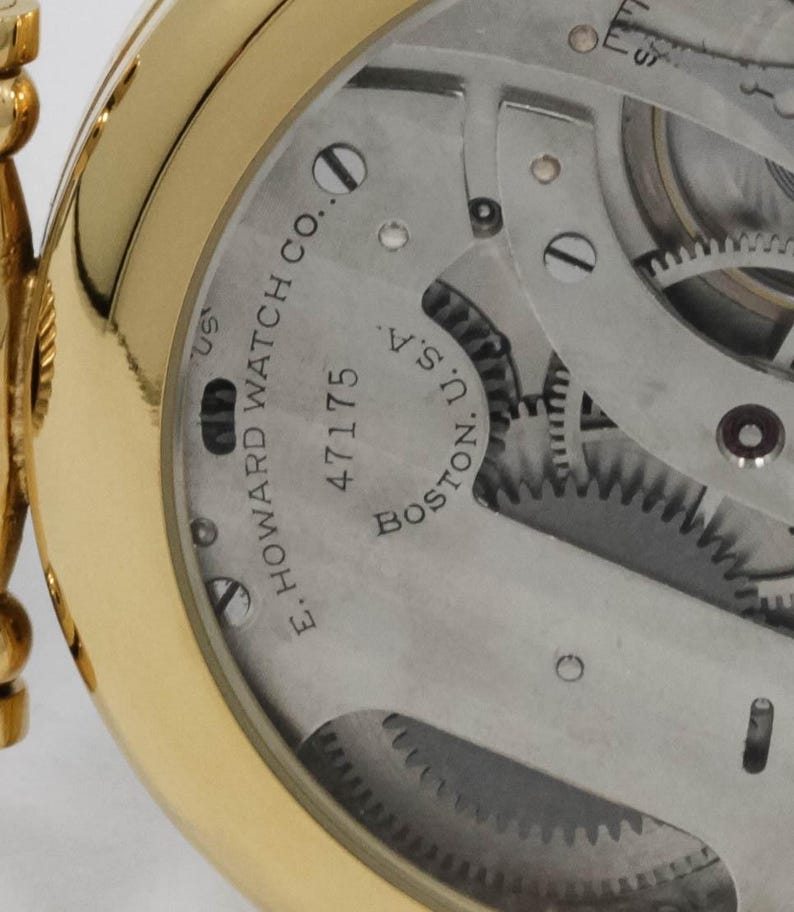 May include: Close-up of a gold pocket watch's inner workings. The watch mechanism is visible, with gears and other components. The text "E. HOWARD WATCH CO. BOSTON. U.S.A." and the number "47175" are printed on the watch face.
