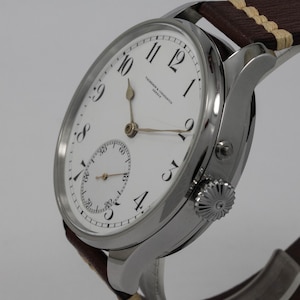 Puede incluir: Un reloj de pulsera plateado con una esfera blanca y marcadores de hora romanos negros. El reloj tiene un peque&ntilde;o subdial en la posici&oacute;n de las 3 en punto y el texto "Vacheron Constantin Geneve" impreso en la esfera.