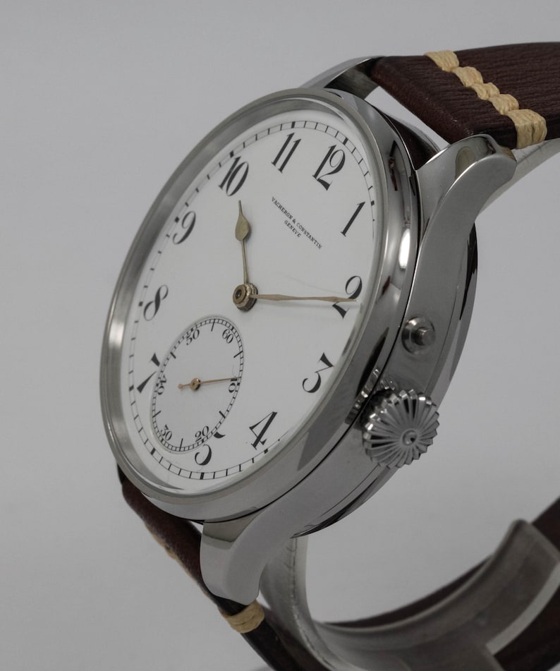 Puede incluir: Un reloj de pulsera plateado con una esfera blanca y marcadores de hora romanos negros. El reloj tiene un peque&ntilde;o subdial en la posici&oacute;n de las 3 en punto y el texto "Vacheron Constantin Geneve" impreso en la esfera.