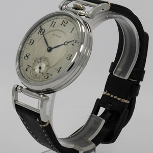 K&ouml;nnte beinhalten: Eine silberfarbene Armbanduhr mit rundem Geh&auml;use und schwarzem Lederarmband. Das cremefarbene Zifferblatt zeigt schwarze arabische Ziffern, d&uuml;nne schwarze Zeiger und ein kleines Hilfszifferblatt auf der Sechs-Uhr-Position. Das Wort HOWARD steht in Schwarz auf dem Zifferblatt.