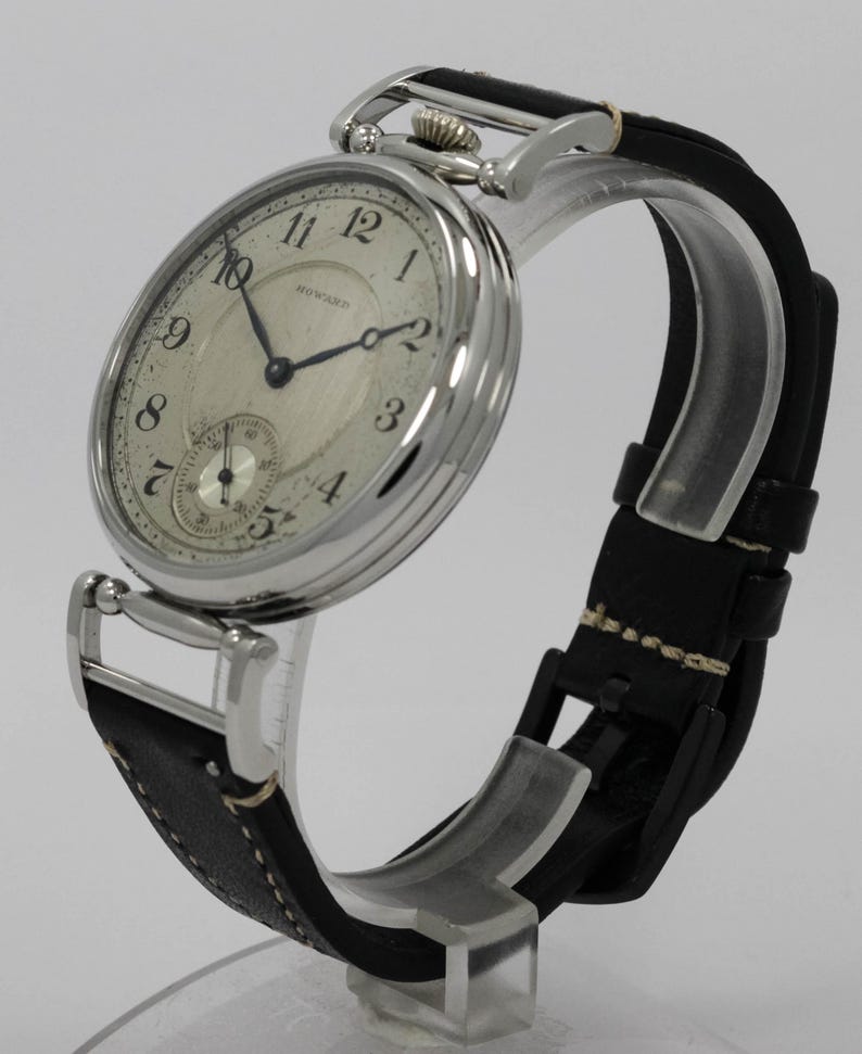 K&ouml;nnte beinhalten: Eine silberfarbene Armbanduhr mit rundem Geh&auml;use und schwarzem Lederarmband. Das cremefarbene Zifferblatt zeigt schwarze arabische Ziffern, d&uuml;nne schwarze Zeiger und ein kleines Hilfszifferblatt auf der Sechs-Uhr-Position. Das Wort HOWARD steht in Schwarz auf dem Zifferblatt.