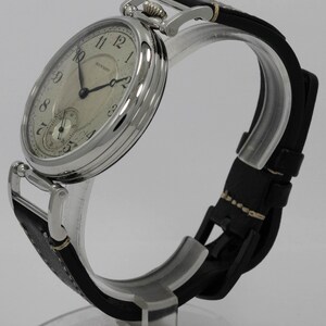 K&ouml;nnte beinhalten: Eine silberfarbene Armbanduhr mit rundem Geh&auml;use und cremefarbenem Zifferblatt mit schwarzen arabischen Ziffern und dem Schriftzug Howard. Die Uhr hat d&uuml;nne schwarze Zeiger, ein kleines Hilfszifferblatt auf der Sechs-Uhr-Position und ein schwarzes Lederarmband.