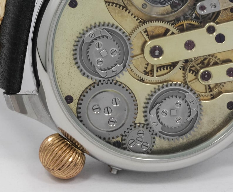 May include: A close-up of a silver pocket watch with a clear face revealing the intricate inner workings of the watch mechanism. The watch has a gold-toned crown and a black leather strap.
