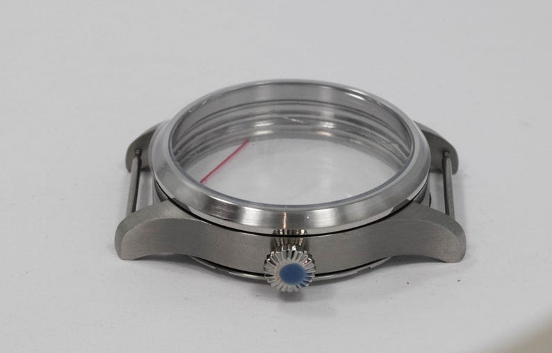 May include: A stainless steel watch case with a clear crystal and a blue-accented crown. The watch case has a round face and is designed to hold the watch movement and dial. The lugs are curved for a comfortable fit.