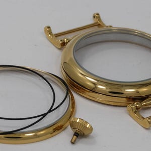 May include: Gold-toned watch case back with a clear glass insert and a black rubber gasket. The case back is separated from the glass insert and gasket. A small gold-toned screw is also included.