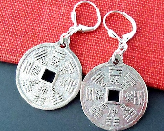 May include: Silver earrings featuring a round coin design with Chinese characters and a square hole in the center. The coins are attached to silver leverback closures.