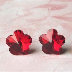 May include: A pair of red flower-shaped crystal earrings. The earrings are small and delicate, and they have a sparkly finish.