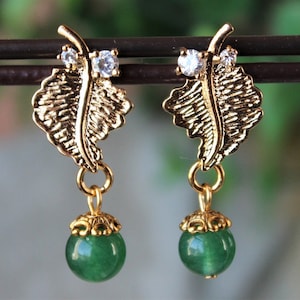 May include: Gold leaf earrings with a green gemstone dangle. The leaf design features two small clear rhinestones.