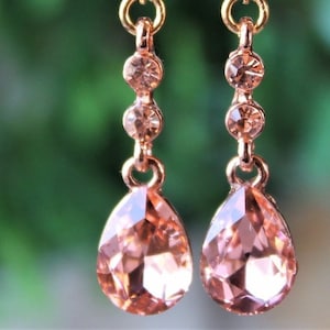 May include: A pair of rose gold dangle earrings with a teardrop-shaped pink crystal and three smaller pink crystals.