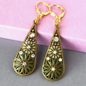 May include: A pair of teardrop-shaped dangle earrings in an antique bronze finish. Each earring features two layered flower motifs in shades of light and dark green enamel, accented with small, clear, iridescent rhinestones and lever-back closures.
