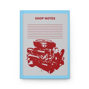 May include: A notebook with a light blue cover and a gray background. The cover features the text "SHOP NOTES" in red, above a red illustration of an engine. The notebook has lined pages.