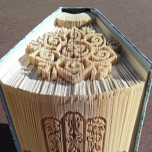 May include: A book with pages folded into a three-dimensional design of a hand. The book is closed and the design is visible on the front cover. The book is titled "Creased Chronicles".
