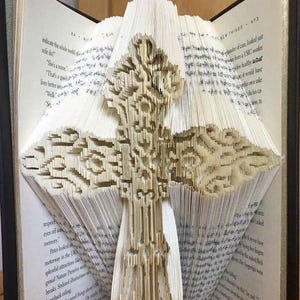 May include: A book with a 3D paper craft of a cross, folded from the pages of the book. The book is open and the cross is standing up. The text "Creased Chronicles" is visible at the bottom of the image.
