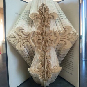 May include: A book folded into the shape of a cross with intricate details. The book is open and the pages are folded to create a three-dimensional design. The title "Creased Chronicles" is visible at the bottom of the image.
