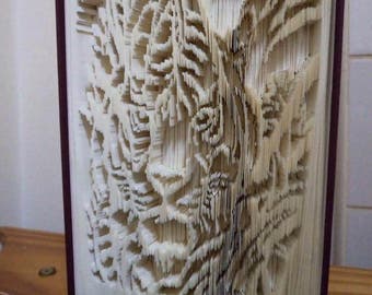 Può includere: Un libro con le pagine piegate e tagliate per creare un design 3D di un albero con foglie. Il libro è rilegato in una copertina di colore rosso scuro e il titolo "Creased Chronicles" è stampato nella parte inferiore della copertina.