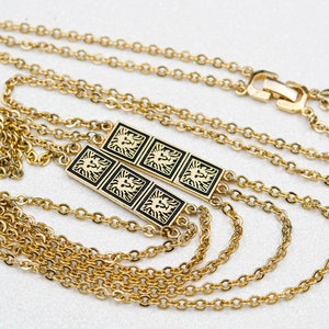 May include: Gold-tone necklace featuring a chain design with two rectangular pendants. Each pendant has a black background with a gold lion emblem. The necklace has a clasp closure.