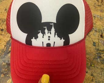 Puede incluir: Gorra de camionero roja y blanca con una silueta negra de la cabeza de Mickey Mouse con la silueta del castillo de Cenicienta dentro de las orejas.