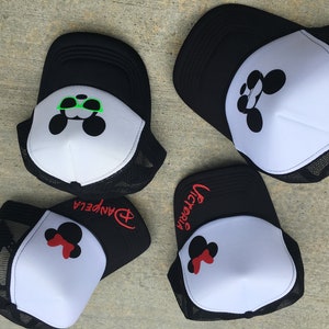 Puede incluir: Cuatro gorras de camionero negras y blancas con un dise&ntilde;o de Mickey Mouse. Las gorras tienen diferentes nombres bordados en ellas: "Victoria", "Danpela" y otras dos. Un Mickey Mouse lleva gafas de sol verdes.