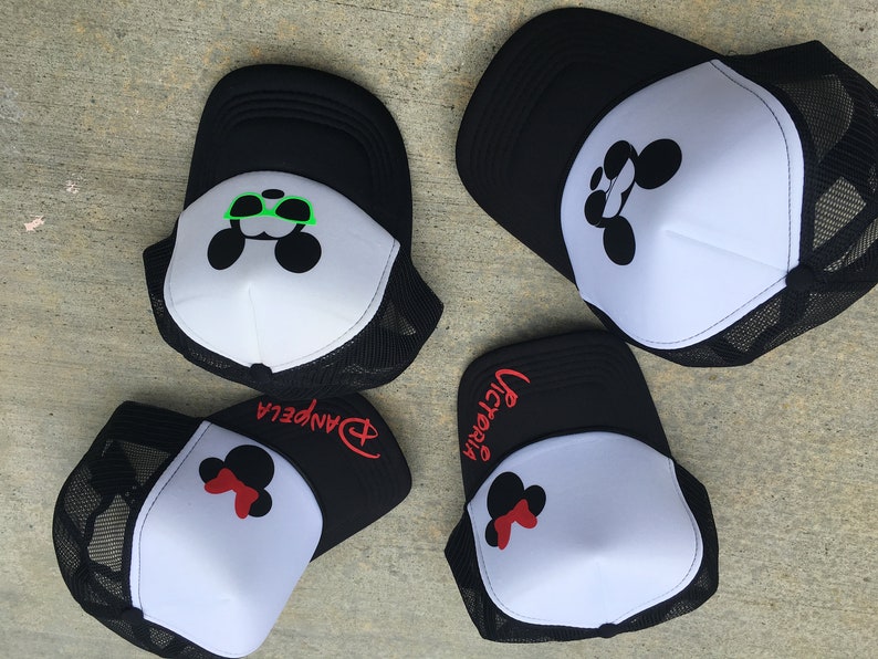 Puede incluir: Cuatro gorras de camionero negras y blancas con un dise&ntilde;o de Mickey Mouse. Las gorras tienen diferentes nombres bordados en ellas: "Victoria", "Danpela" y otras dos. Un Mickey Mouse lleva gafas de sol verdes.