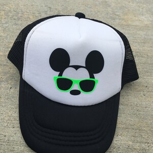Puede incluir: Una gorra de camionero Mickey Mouse en blanco y negro con gafas de sol verdes. La gorra tiene una parte trasera de malla negra y una parte delantera blanca.