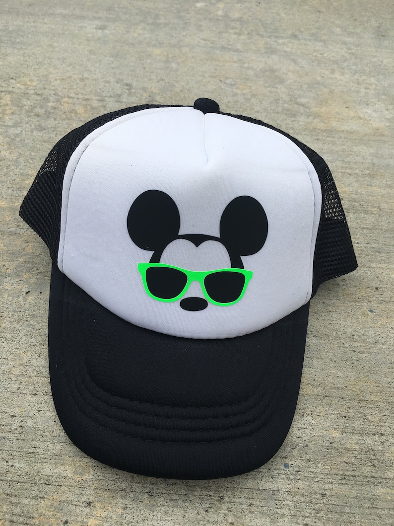 Puede incluir: Una gorra de camionero Mickey Mouse en blanco y negro con gafas de sol verdes. La gorra tiene una parte trasera de malla negra y una parte delantera blanca.