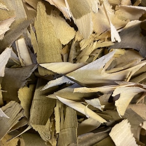 May include: A close-up of a pile of wood shavings. The shavings are light brown and have a rough texture.
