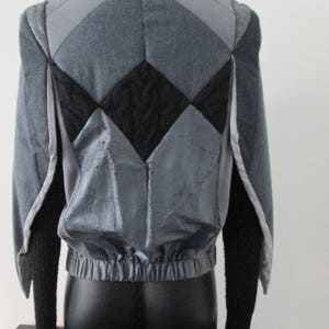 Puede incluir: Una chaqueta acolchada gris y negra con cierre de cremallera y mangas largas. La chaqueta tiene un patrón de diamante único en la espalda.