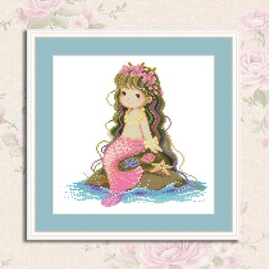 May include: A cross-stitch pattern featuring a mermaid with pink and purple scales, sitting on a rock with a flower crown. The mermaid has long brown hair and is surrounded by blue and green water.