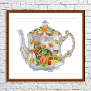 May include: A white teapot with a gold trim decorated with fall leaves, pumpkins, and a cornucopia overflowing with fruit and vegetables.