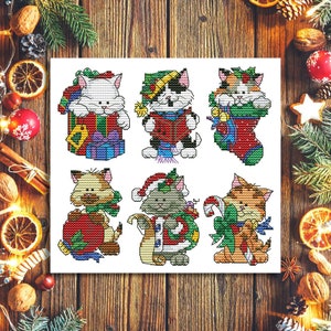 Puede incluir: Seis patrones de punto de cruz con gatos vestidos con atuendos festivos navideños. Los gatos sostienen regalos, bastones de caramelo y llevan gorros de Papá Noel.