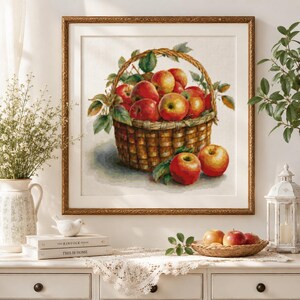 May include: A framed cross-stitch artwork depicting a woven basket filled with red and yellow apples, with additional apples resting at the base. The piece is rendered in detailed needlework, showcasing vibrant fruit colors and green leaves.