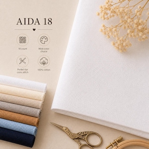 May include: Aida 18 cross-stitch fabric in white, with a stack of colored fabric swatches. The image includes text that reads "AIDA 18", "18 count", "Wide color choice", "100% cotton". A pair of gold scissors and a wooden embroidery hoop are also visible.