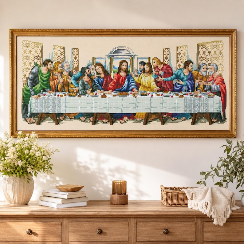 May include: A framed cross-stitch embroidery depicting The Last Supper, featuring Jesus and the twelve disciples seated at a long table covered with a white cloth, set against a light background within a decorative gold-colored rectangular frame.